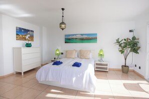 A bedroom with a bed, two bedside tables, a dresser, a hanging lamp, a potted plant, and two wall-mounted paintings.
