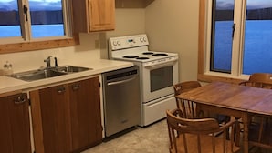 A kitchen with wooden cabinets, a stove, a sink, and a dining table with chairs. - 10 Minutes From Waterton Park Boundary Lakeside Gallery & Guest House (Mountain View)