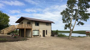 A two-story building with a wooden staircase leading to a balcony, a stone wall, and a view of a lake. - 10 Minutes From Waterton Park Boundary Lakeside Gallery & Guest House (Mountain View)