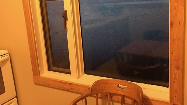 A room with a wooden table and chair, a window with a view of a body of water, and a white appliance in the corner. - 10 Minutes From Waterton Park Boundary Lakeside Gallery & Guest House (Mountain View)
