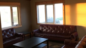 A living room with a high ceiling, a ceiling fan, a brown leather sofa, a coffee table, and large windows. - 10 Minutes From Waterton Park Boundary Lakeside Gallery & Guest House (Mountain View)