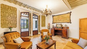 A spacious living room with a large chandelier, a sofa set, a wooden coffee table, and a painting on the wall.