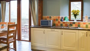 A kitchen with white cabinets, a microwave, and a window with a view of a wooden deck. - 4 bedroom accommodation in Soar, near Brecon (Soar, near Brecon)