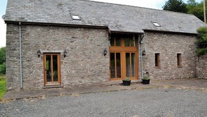 A stone building with a sloped roof, a wooden door, and two windows. - 4 bedroom accommodation in Soar, near Brecon (Soar, near Brecon)