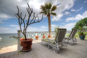 Una terraza de madera con dos sillones de descanso, una palmera y vista al océano.