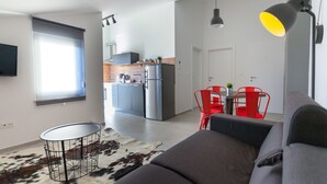 A modern living room with a grey sofa, a cowhide rug, a dining table with red chairs, a kitchen in the background, and a mounted TV.