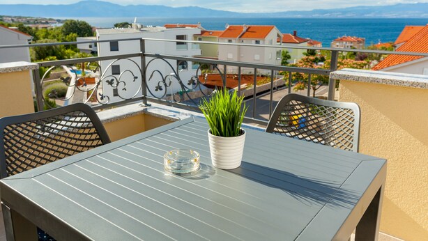 A balcony with a metal table, two chairs, a potted plant, and a clear glass ashtray.