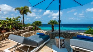 A beachside lounge with two lounge chairs, a blue umbrella, and a view of the ocean.