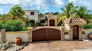 A house with a stone gate, palm trees, and a tiled roof.