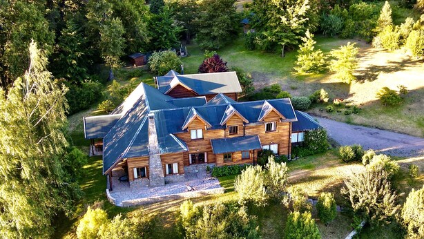 Une grande cabane en bois à plusieurs étages, dotée d’un toit en pente et entourée d’une forêt dense.