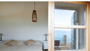 A bedroom with a large bed, two bedside tables, a hanging light fixture, and a view of the sea through a large window. - Amazing seafront setting-Infinity pool (Sumartin)