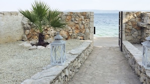 A pathway leading to a beach with stone walls and lanterns. - Amazing seafront setting-Infinity pool (Sumartin)