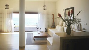 A modern living room with a sofa, a coffee table, and a vase with flowers. There is a view of the ocean through sheer curtains. - Amazing seafront setting-Infinity pool (Sumartin)