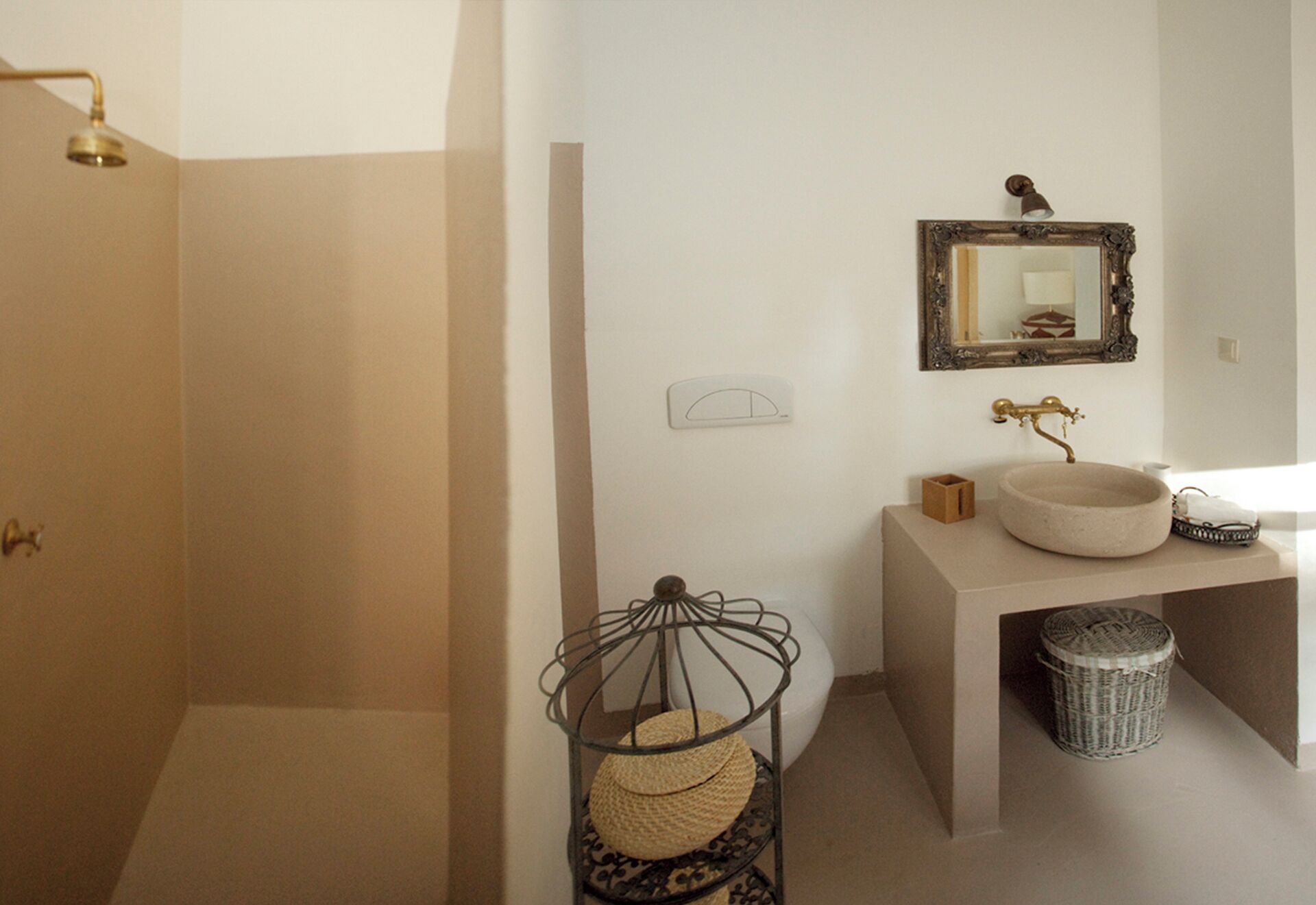 A bathroom with a shower, a sink with a vintage faucet, a mirror, and a wicker basket.
