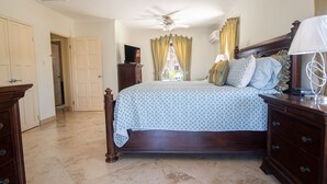 Un dormitorio con una cama, ventilador de techo, cómoda y televisor sobre un mueble.