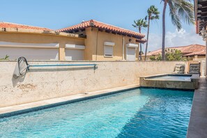 A swimming pool with a tiled deck, a palm tree, and a building with a tiled roof.