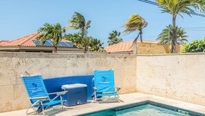 Una piscina con dos sillas reclinables azules y un enfriador.