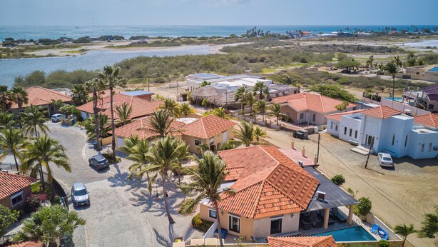 Zona residencial costera con casas de techo rojo, piscina y palmeras.
