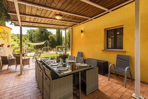 An outdoor patio with a dining table set for four, surrounded by wicker chairs, a pool in the background, and a yellow wall. - Luxury Tuscan Hideaway with Heated Swimming Pool (Chiusi)