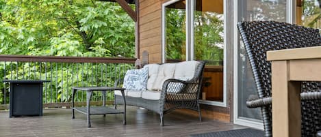 A covered deck with a wicker sofa, a small table, and a trash bin.