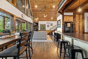 A spacious kitchen with wooden beams, a dining area with a long table and chairs, and a cozy living area with a sofa and fireplace.