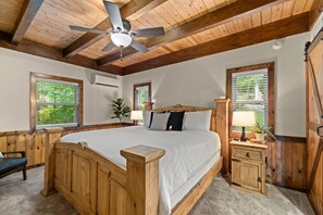 A wooden bedroom with a bed, bedside tables, a ceiling fan, and windows with blinds.