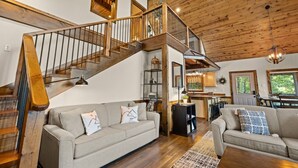 Un salon spacieux avec un escalier en bois, deux canapés, un coin repas et une cuisine.