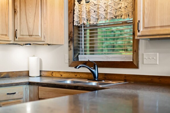 A kitchen with wooden cabinets, a stainless steel sink, and a macrame curtain over the window.