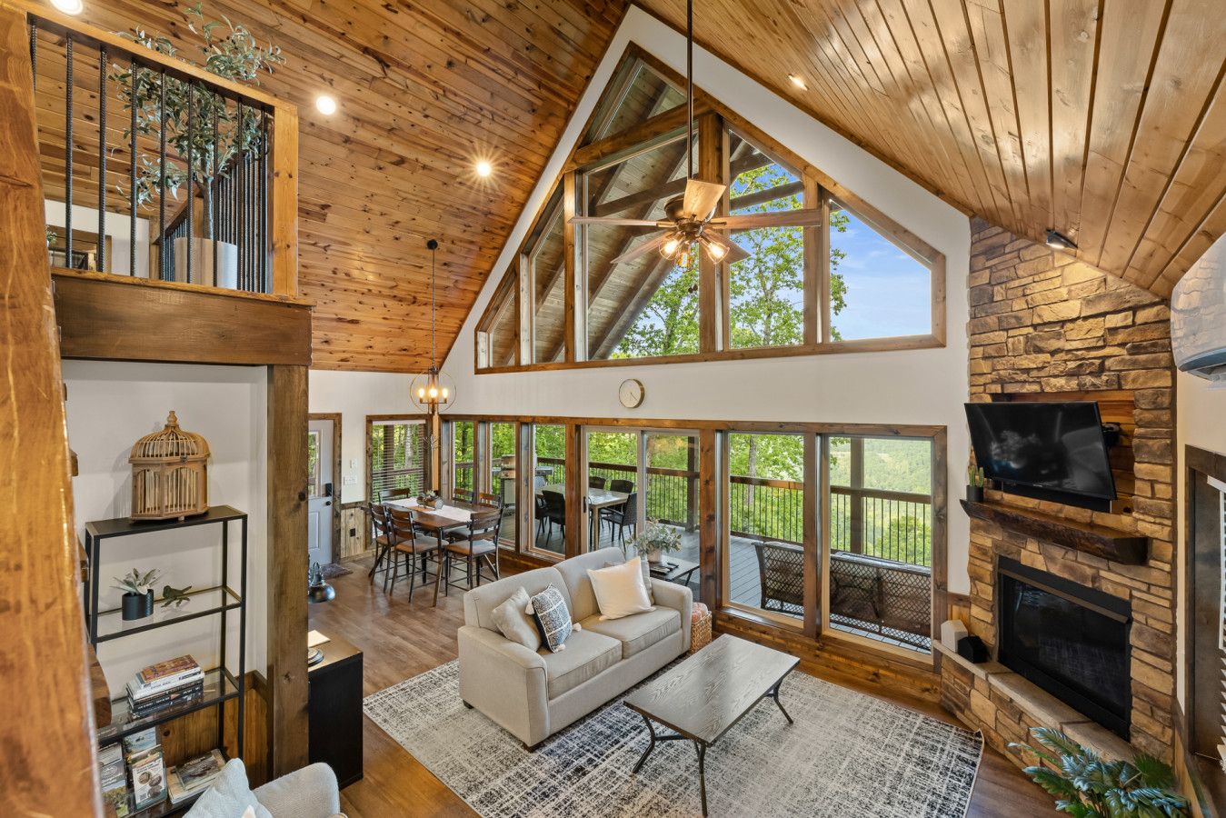 A spacious living area with a high ceiling, wooden beams, a fireplace, and large windows offering a view of the outdoors.