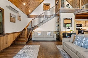 A spacious living area with a wooden staircase, a sofa, and a kitchen area. - Mountain Crest Cabin-Relaxing Vacation in Jasper (Jasper)