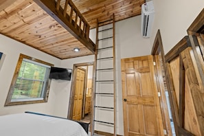 A bedroom with a wooden ceiling, a ladder, a window with blinds, a bed, and an air conditioning unit. - Mountain Crest Cabin-Relaxing Vacation in Jasper (Jasper)