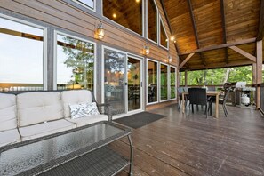 A covered outdoor area with a wooden deck, a sofa with cushions, a table, and chairs. - Mountain Crest Cabin-Relaxing Vacation in Jasper (Jasper)
