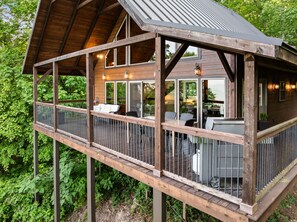 A wooden deck with outdoor seating and a covered area, surrounded by greenery.