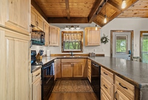 A kitchen with wooden cabinets, a granite countertop, a built-in dishwasher, and a window with a view of greenery.