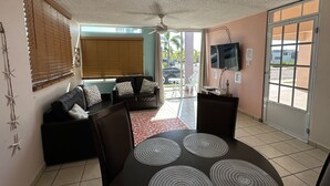 Un salon comprenant un canapé, des fauteuils, un téléviseur et un coin repas avec une table et des sets de table.