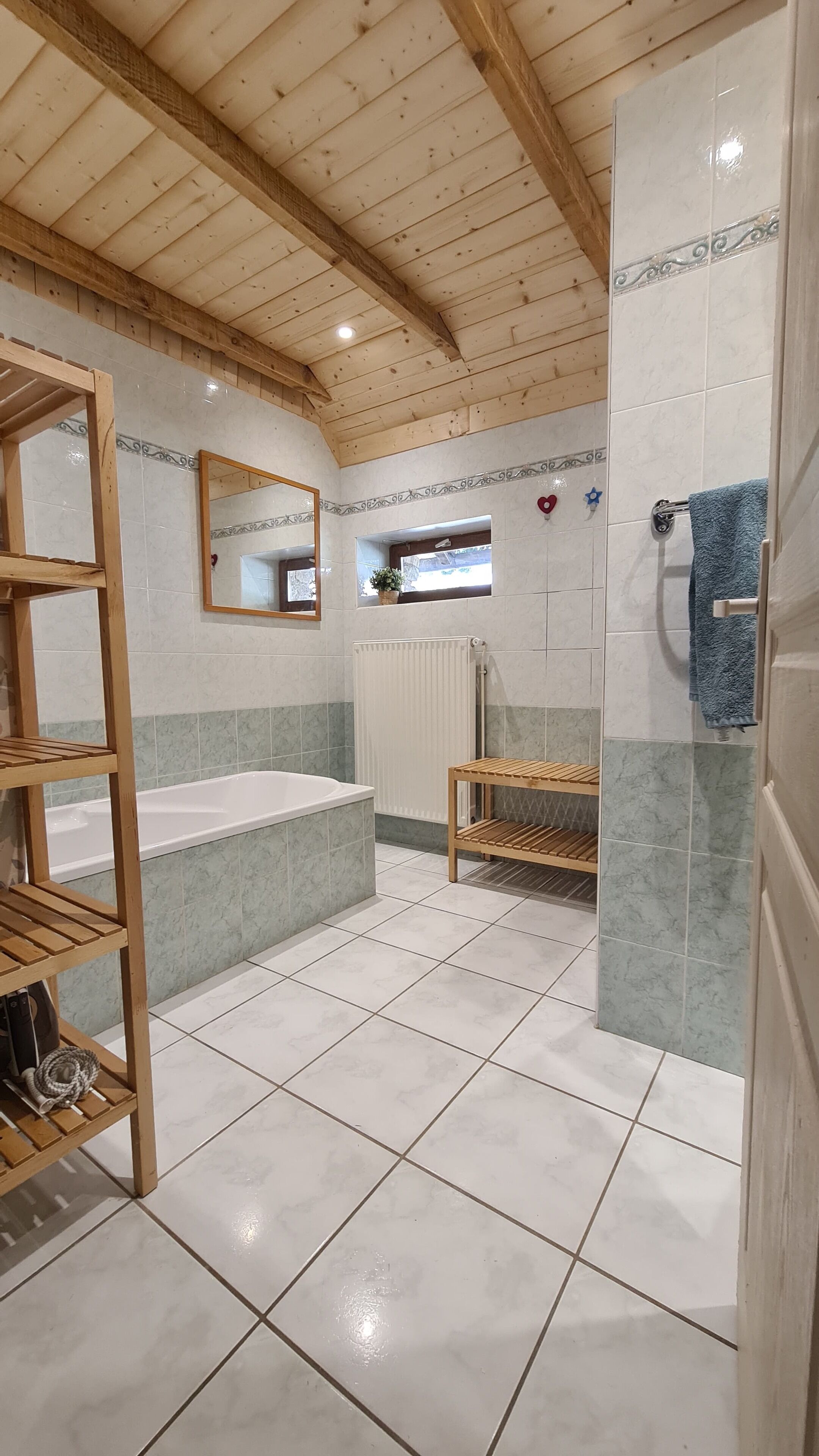 Un baño con techo de madera, una bañera, un estante de madera, un espejo, un perchero y un radiador.