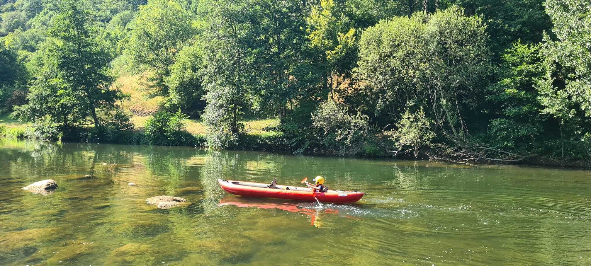 A red canoe on a calm river surrounded by dense greenery.