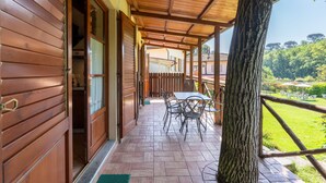 Un patio coperto con tavolo e sedie di legno, un tronco d'albero e vista su un paesaggio verde.
