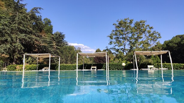 Una piscina blu cristallina con tre ombrelloni e lettini.