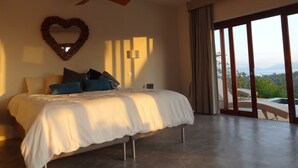 Ein Schlafzimmer mit einem Bett, einem Deckenventilator, einer herzförmigen Dekoration und Blick ins Freie.
