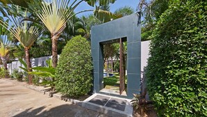 Un edificio moderno con una entrada geométrica, rodeado de exuberante vegetación y palmeras.