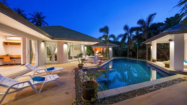 Una casa moderna con piscina, mobiliario de exterior y un patio bien iluminado.