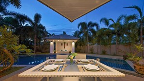 Un comedor con piscina, rodeado de palmeras y una zona de estar cubierta.