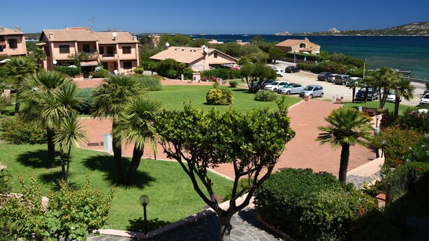 A coastal residential area with multiple two-story houses, a parking lot, and a clear view of the sea. - Seafront house with garden (Cannigione)