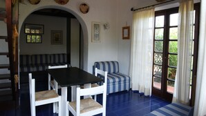 A room with a dining table, chairs, a striped sofa, and a large arched doorway. - Seafront house with garden (Cannigione)