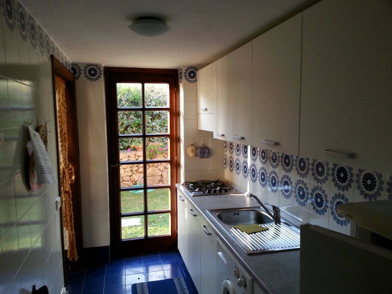 Une cuisine équipée d’une cuisinière à gaz, d’un évier et de placards. Une fenêtre offre une vue sur la verdure environnante.