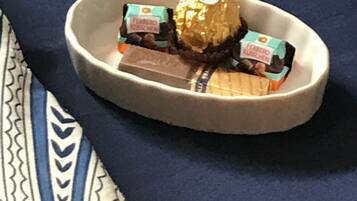 A bed with a blue and white patterned bedspread and a beige tray holding a Ferrero Rocher chocolate and two Ferrero Kauffmann chocolates.