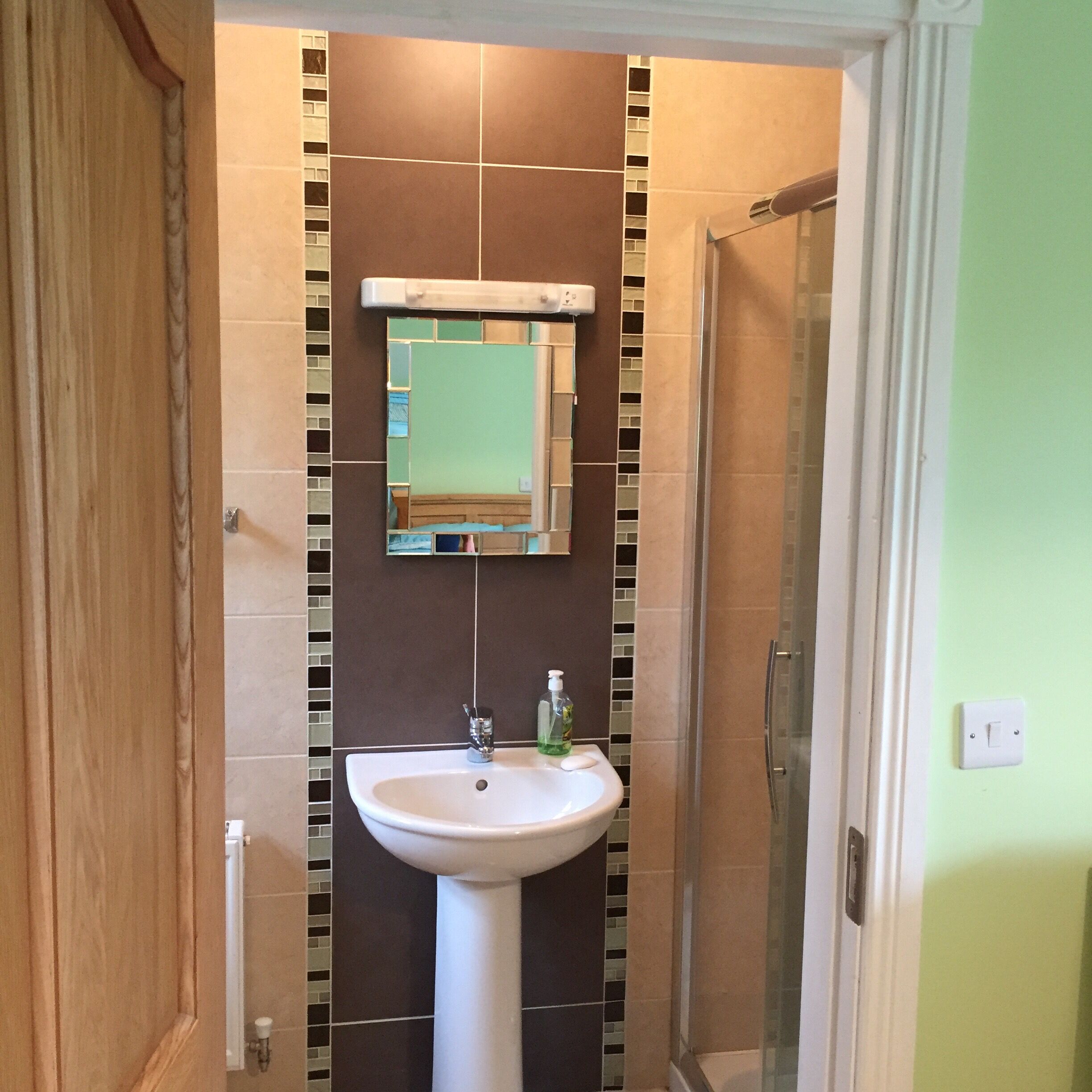 A bathroom with a white pedestal sink, a mirror above it, and a shower area to the right.