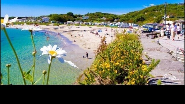 Una playa con agua cristalina, gente y vegetación al fondo.