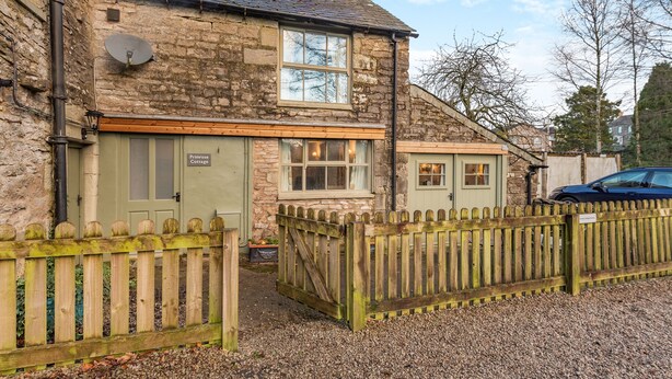 A stone cottage with a green door labeled 'Primrose Cottage,' a wooden fence, and a gravel driveway. - 1 bedroom accommodation in Shap, near Penrith (Shap, near Penrith)